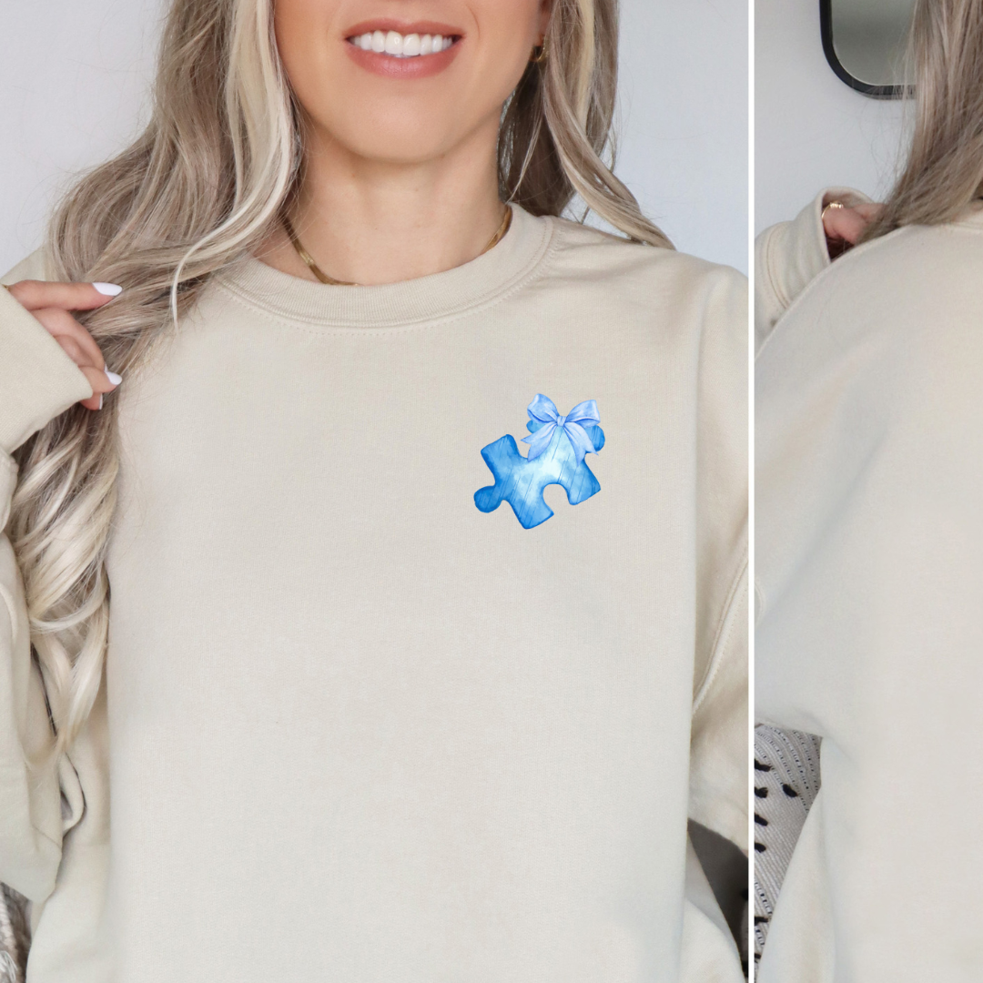 Sand colored sweatshirt with a soft blue puzzle piece  with a bow on the left chest. 