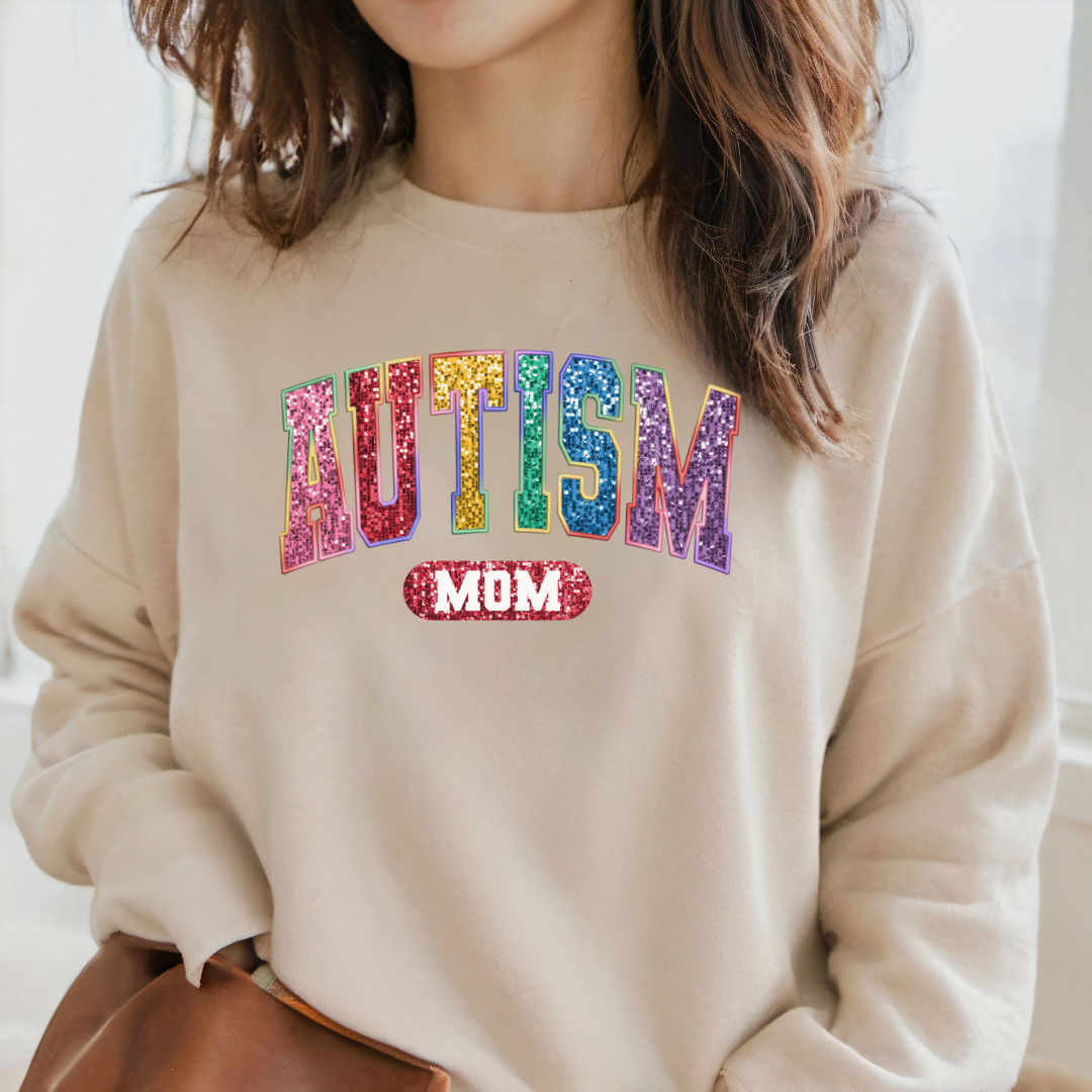 A view of a lady wearing a Sand colored sweatshirt with the word Autism mom printed on the front. Using faux sequins.